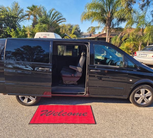 Black 7-seater passenger van with sliding door open and a red welcome mat