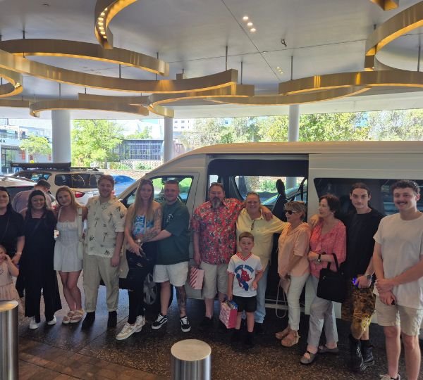 Family group gathered in front of a Perth Mini Charter minibus at a hotel entrance