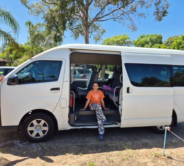 Passenger sitting in the open side door of a white Toyota HiAce minibus