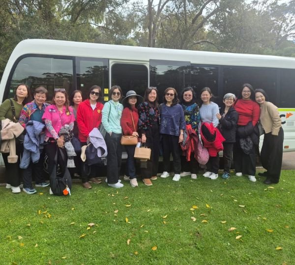 Group of tourists posing on the grass in front of a minibus during a Perth sightseeing tour